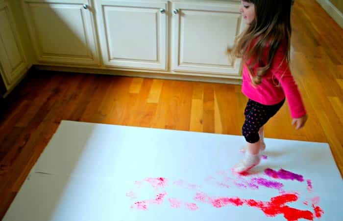 niña dejando huellas colores con sus pies en un papel puesto en el suelo jugar a dejar huellas de colores en un papel