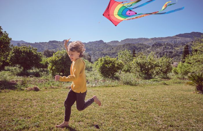 niño volando una cometa multicolor por el campo Juegos tradicionales: cometa