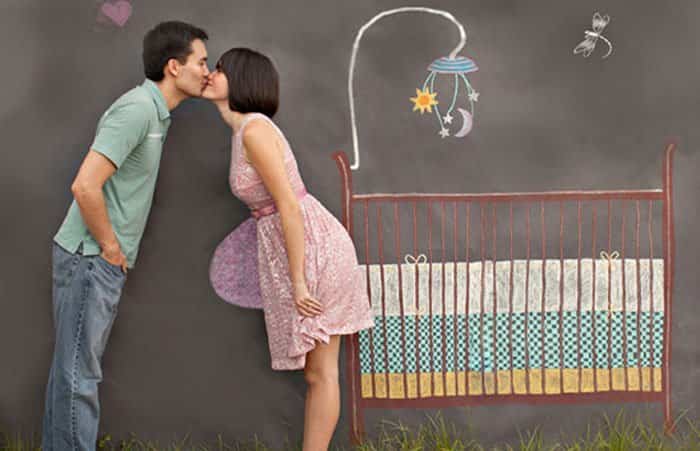 La pareja se besa ante un escenario dibujado en una pizarra Foto de los futuros padres sobre fondo de pizarra con cuna dibujada