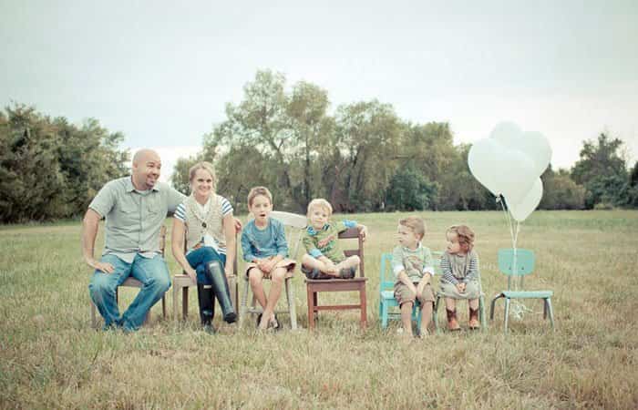Foto de familia anunciando la llegada de un nuevo miembro La familia sentada en varias sillas, la última vacía y con globos