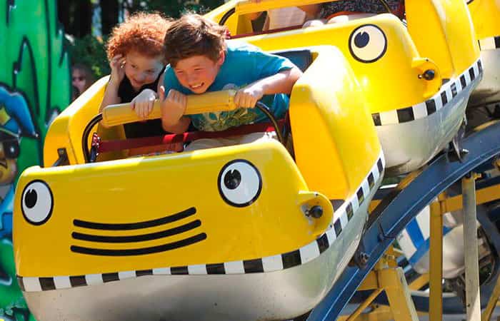 Niños montados en una atracción tipo montaña rusa Planes con niños: Al parque de atracciones