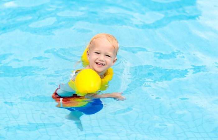 Niño sonriente camina por piscina con chaleco salvavidas haciendo que es un barco Zona permitida, jugando a ser un barco