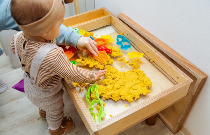 Niña jugando en mesita con plastilina casera teñida de amarillo Plastilina casera para despertar el sentido del tacto