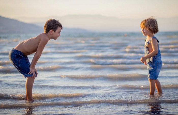 Coger a un bebé en brazos favorece sus habilidades sociales en el futuro Dos niños juegan en la orilla del mar. Coger a un bebé en brazos les da seguridad