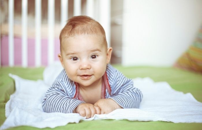 bebé tumbado boca abajo, apoyado en sus brazos, mira a la cámara Nombres raros de niños para tu bebé