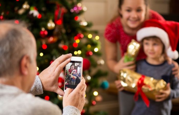 padre haciendo una foto a sus dos hijos junto al arbol de navidad planes para diciembre fotos familiares