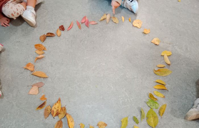 Niños con círculo de hojas de otoño en el suelo Aprendizajes significativos con actividaes al aire libre