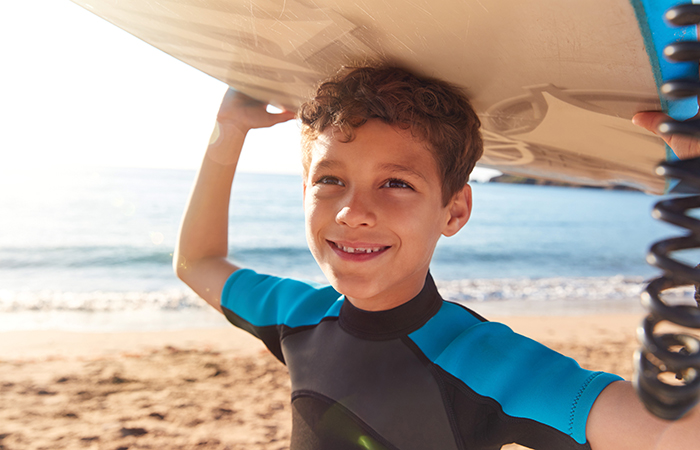 niño en la playa llevando la tabla de surf sobre su cabeza Berlitz Camps: surf
