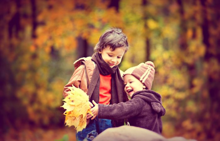 Dos hermanos jugando con hojas de otoño. Aprendizaje y juego aprender de los hermanos mayores
