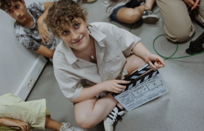 Grupo de adolescentes en clase de cine y chica con claqueta en la mano Campamento de cine ECAM 2024: el grupo de los más mayores