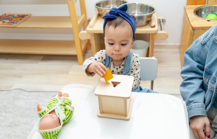 Niña pequeña jugando con una caja de permanencia Montessori sencilla Caja de permanencia Montessori: Juguete de madera con orificios