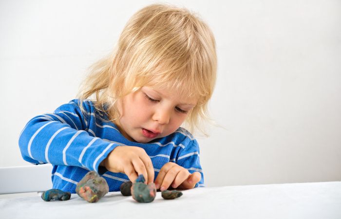 Niño pequeño formando bolitas de plastilina, uno de los juegos para dejar el pañal Juegos con plastilina para deja el pañal