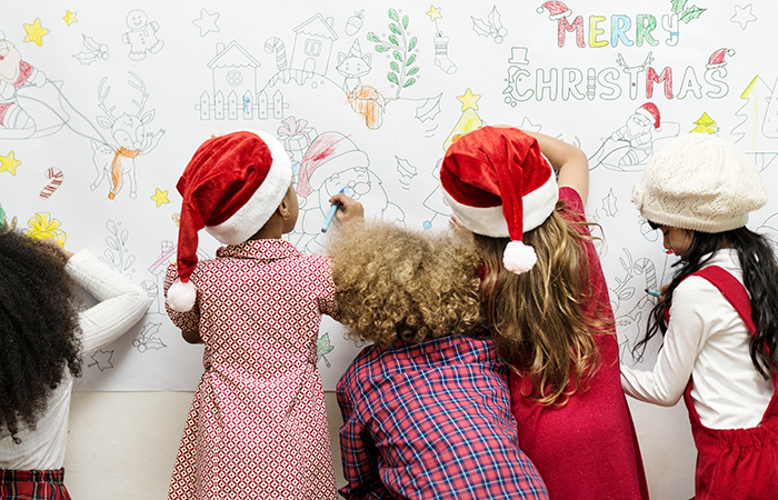 Niños y niñas de espaldas pintando en un mural navideño Trabajar los valores de la navidad:paz